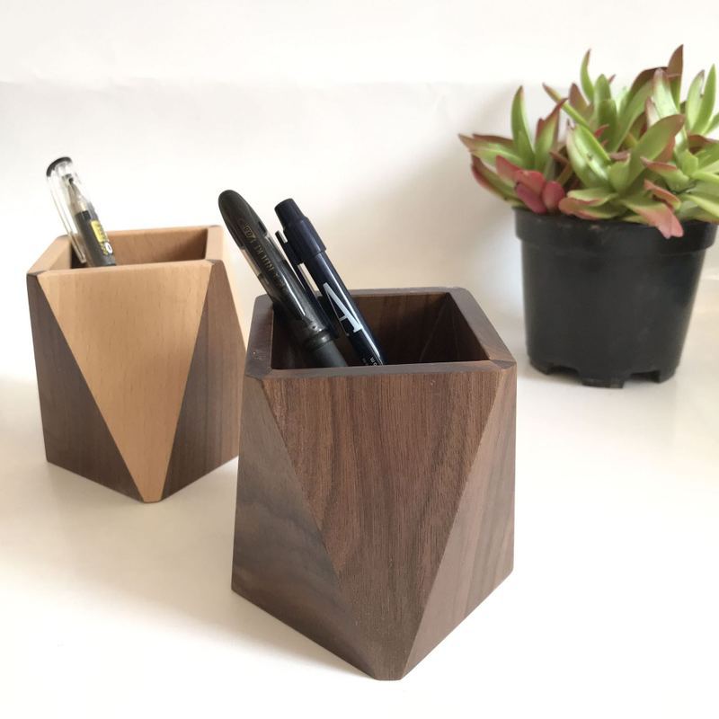 Angular wooden pen holders filled with pens next to a succulent plant on a desk