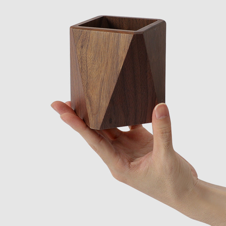 Hand holding a compact square wooden pen holder to show its size