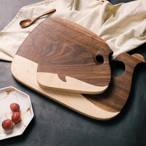 Black walnut whale-shaped cutting boards styled on a table with fruit and a spoon